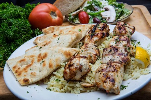 Grilled chicken skewers served with rice, pita bread, a fresh salad, and a slice of tomato.