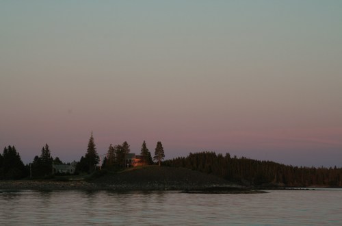 A serene landscape at dusk featuring a shoreline, trees, and a house illuminated by soft evening light.