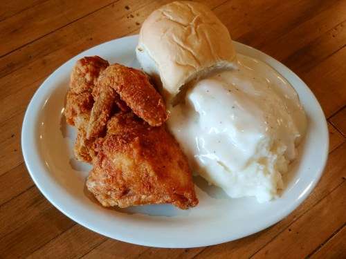 A plate of fried chicken wings, creamy mashed potatoes with gravy, and a soft dinner roll on a wooden table.