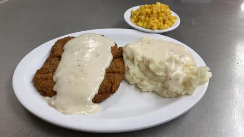 A plate of fried chicken smothered in gravy, served with mashed potatoes and corn on the side.