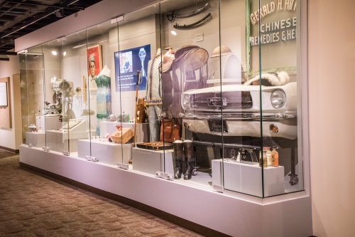 Display case featuring vintage clothing, a classic car, and various artifacts in a museum setting.