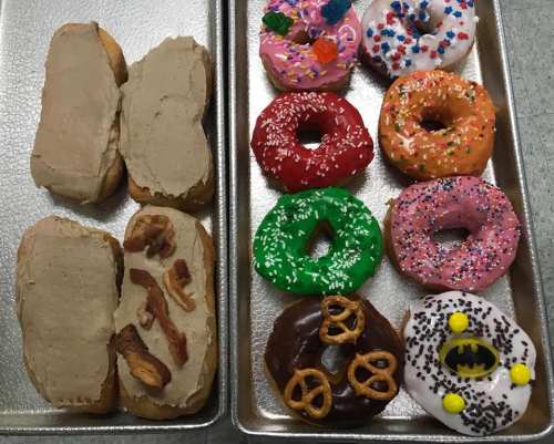 Two trays of colorful donuts: one with frosted varieties and the other featuring a bacon-topped donut.
