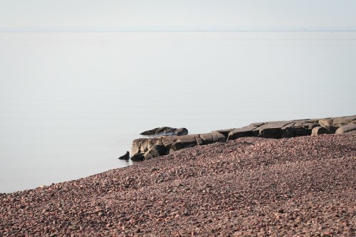 A calm shoreline with smooth rocks and a pebbly beach, reflecting a serene, tranquil atmosphere.