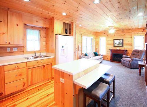 Cozy wooden cabin interior featuring a kitchen, living area, and a fireplace with natural light from large windows.