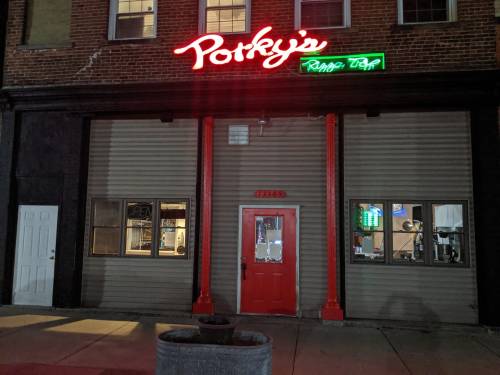 A brick building with a neon sign reading "Porky's" and a red door, illuminated at night.