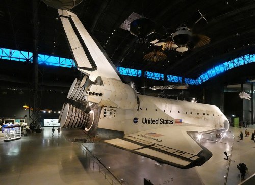 Space shuttle on display in a museum, showcasing its engines and tail, with exhibits in the background.