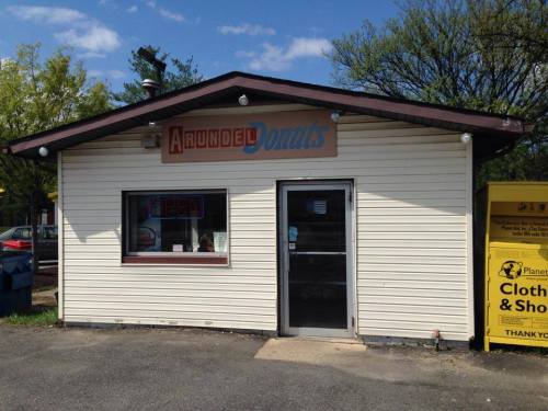 A small, single-story donut shop with a sign reading "Arundel Donuts" and an open sign in the window.