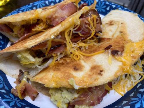 A plate of crispy quesadillas filled with cheese, bacon, and scrambled eggs, garnished with melted cheese.