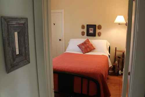 Cozy bedroom with a double bed, orange quilt, decorative pillow, and soft lighting from a wall lamp.