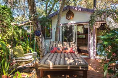 Cozy outdoor seating area with a striped lounge, surrounded by lush greenery and a charming cottage in the background.