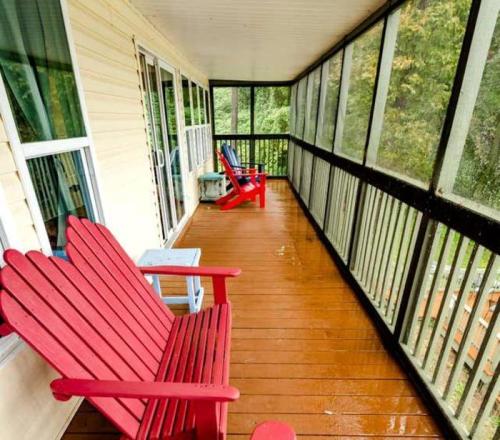 A screened porch with red and blue chairs overlooking a green landscape, featuring wooden flooring.