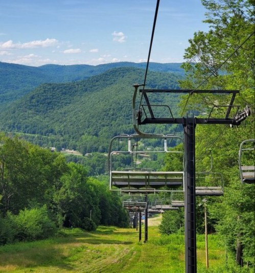 A scenic view of a ski lift with empty chairs, surrounded by lush green mountains and a clear blue sky.