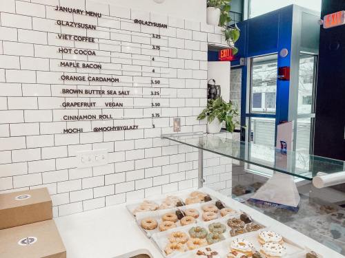 A menu on a tiled wall featuring various food items and prices, with a display of donuts in the foreground.
