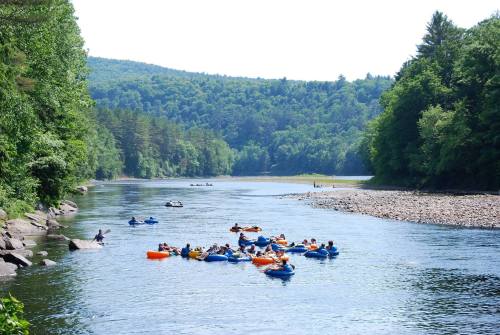 A group of people floating on colorful rafts in a serene river surrounded by lush green trees and hills.