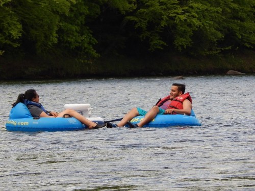 Two people relax on inflatable tubes in a river, surrounded by lush greenery.