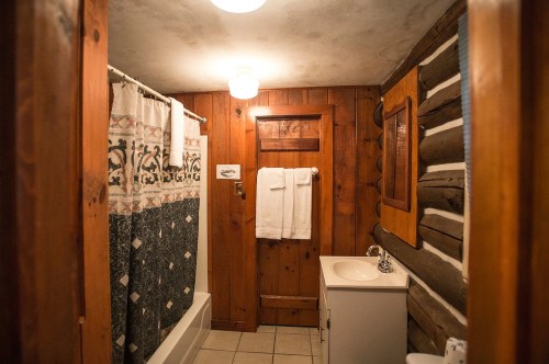 Cozy bathroom with wooden walls, a shower curtain, towels, and a sink, featuring rustic decor and warm lighting.