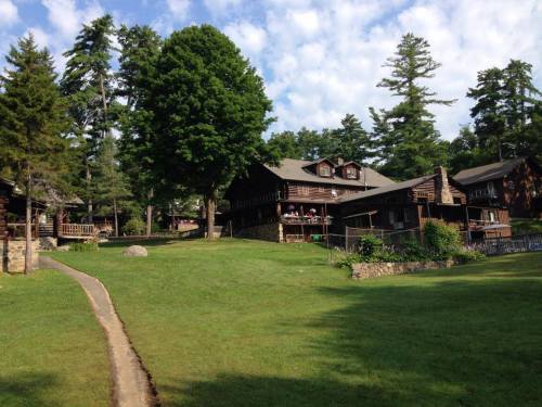 A scenic view of rustic cabins surrounded by lush green trees and a clear blue sky.