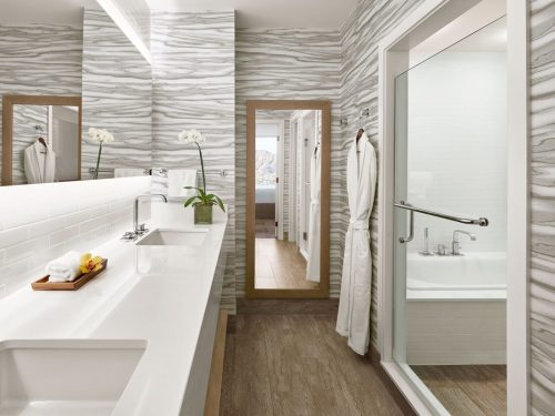 Modern bathroom with a sleek vanity, large mirror, and a glass shower, featuring elegant gray wave-patterned walls.