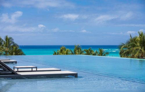 A serene infinity pool overlooking a turquoise ocean and palm trees under a clear blue sky.