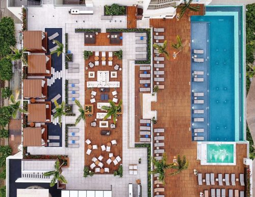 Aerial view of a modern hotel rooftop with a pool, lounge areas, and greenery.