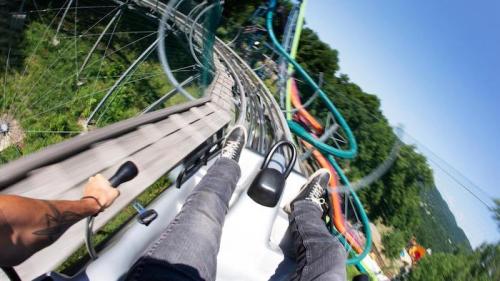 A thrilling view from a roller coaster, showing feet and track as it twists through a lush green landscape.