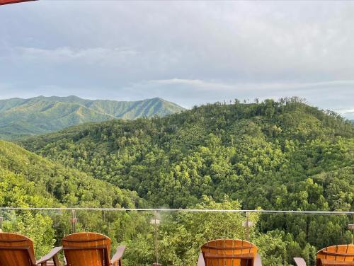A scenic view of lush green mountains under a cloudy sky, with wooden chairs in the foreground.