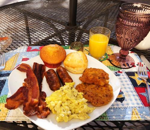 A plate of breakfast featuring scrambled eggs, bacon, sausage, a muffin, a biscuit, and a glass of orange juice.