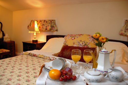 A cozy bedroom with a neatly made bed, a vase of flowers, and a breakfast tray featuring juice and fruit.