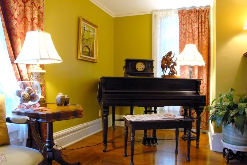 A cozy room featuring a black piano, decorative lamps, a clock, and elegant curtains against a green wall.