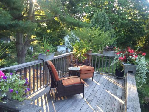 A cozy wooden deck with two chairs, a small table, and vibrant flowers in planters, surrounded by greenery.
