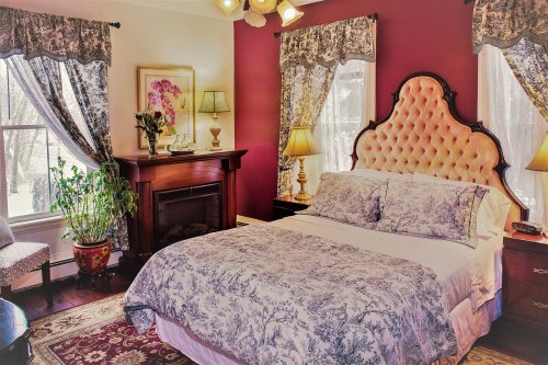 Cozy bedroom with a tufted headboard, floral bedding, elegant curtains, and a fireplace, creating a warm atmosphere.