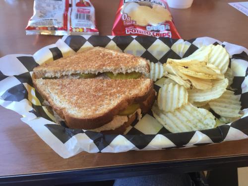 A toasted sandwich with pickles, served with ridged potato chips in a checkered basket.