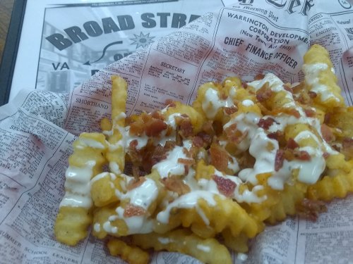Crispy crinkle-cut fries topped with bacon bits and drizzled with creamy sauce, served in a paper-lined basket.