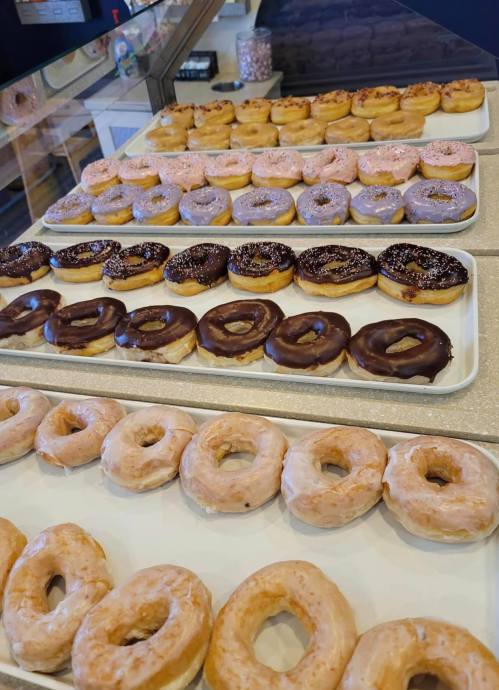 A display of assorted donuts in various flavors and toppings, arranged on white trays.
