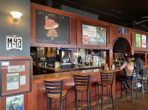 A cozy bar with a wooden counter, colorful posters, and patrons enjoying drinks in a warm, inviting atmosphere.