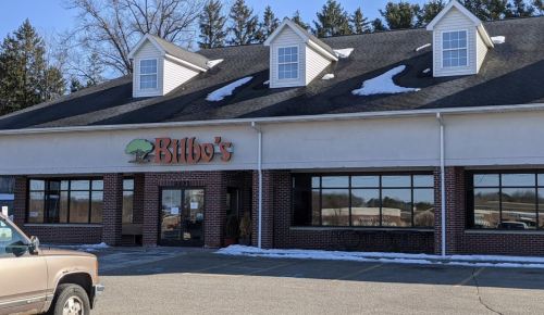 Exterior of Bilbo's restaurant, featuring a sign and large windows, with snow on the roof and a parked truck in front.