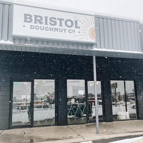 Exterior of Bristol Doughnut Co. building with a snowy scene and large windows showcasing the shop's name.