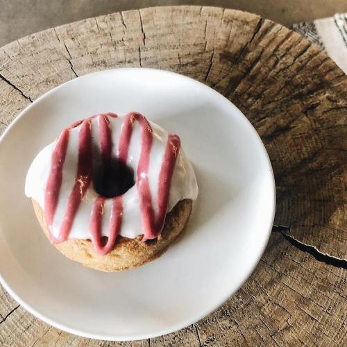 A glazed donut with white icing and red drizzle on a small white plate, resting on a wooden surface.