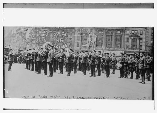 A British band performs "Star Spangled Banner" in a parade in Detroit, with musicians and banners in the background.