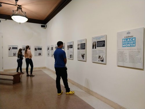 Visitors observe exhibits celebrating Black History Month in a gallery with informative panels on the walls.
