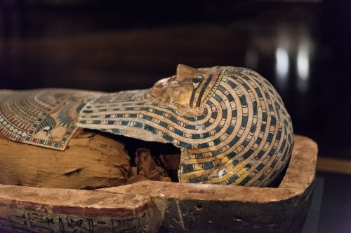 Ancient Egyptian sarcophagus with a decorated lid, revealing a wooden mummy inside.