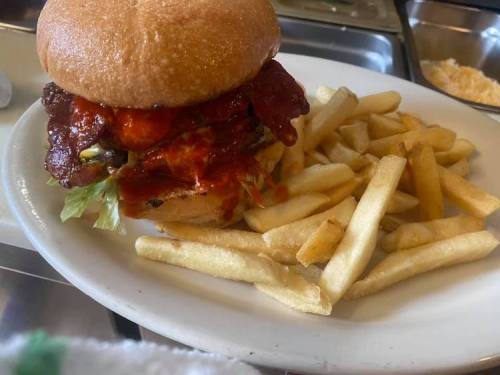 A close-up of a burger with crispy bacon, lettuce, and sauce, served with a side of golden French fries.