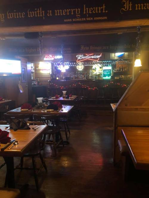 Cozy restaurant interior with wooden tables, bar area, and festive decorations, including neon signs and holiday lights.