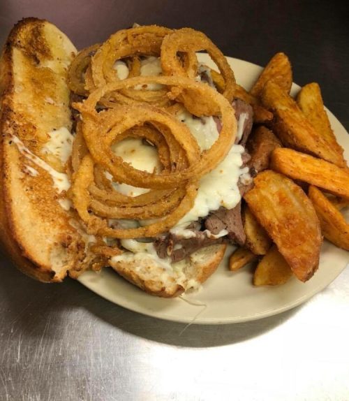 A hearty sandwich with roast beef, melted cheese, and crispy onion rings, served with golden potato wedges.
