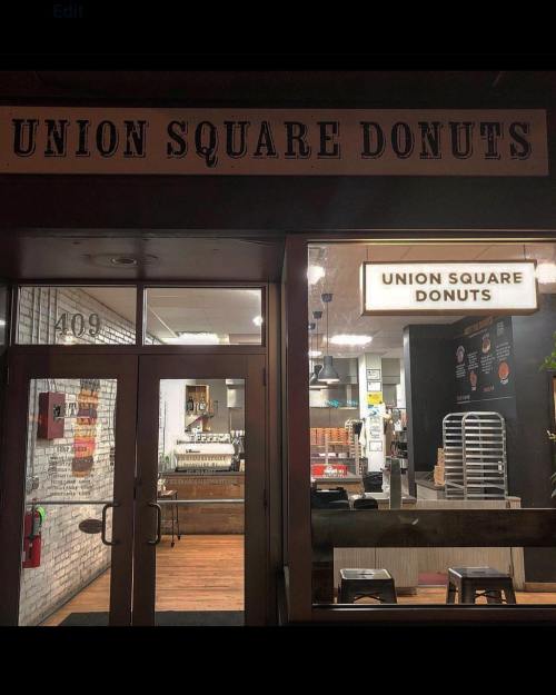 Exterior view of Union Square Donuts shop at night, featuring a sign and large windows showcasing the interior.