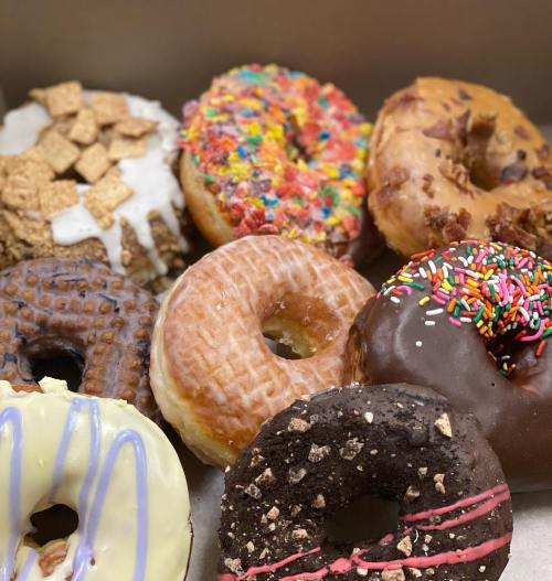 A variety of colorful donuts with different toppings, including sprinkles, cereal, and chocolate, arranged in a box.