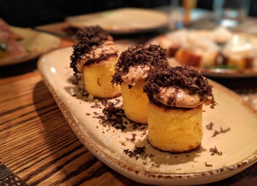 Three small, round cakes topped with creamy frosting and chocolate shavings, served on a beige plate.