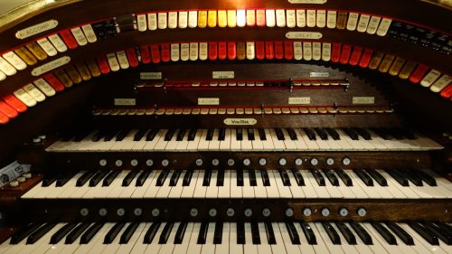 Close-up of a vintage organ console featuring multiple keyboards and colorful stop buttons.