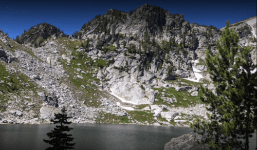 A serene mountain landscape featuring rocky cliffs and a calm lake surrounded by greenery.