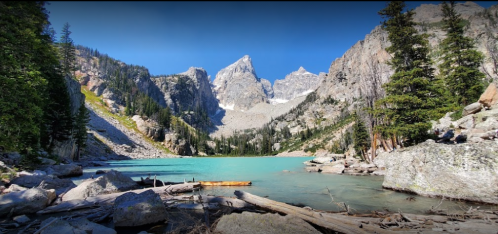 A serene mountain lake surrounded by towering peaks and lush greenery under a clear blue sky.